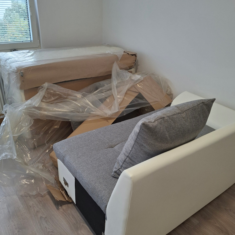 Kotna usnjena sedežna za dnevno sobo v beli barvi z sivimi blazinami pred sestavo