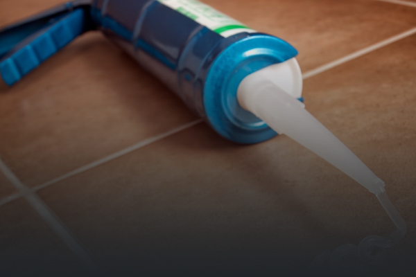 Modra pištola za silikon s prozornim silikonom na rjavih ploščicah.